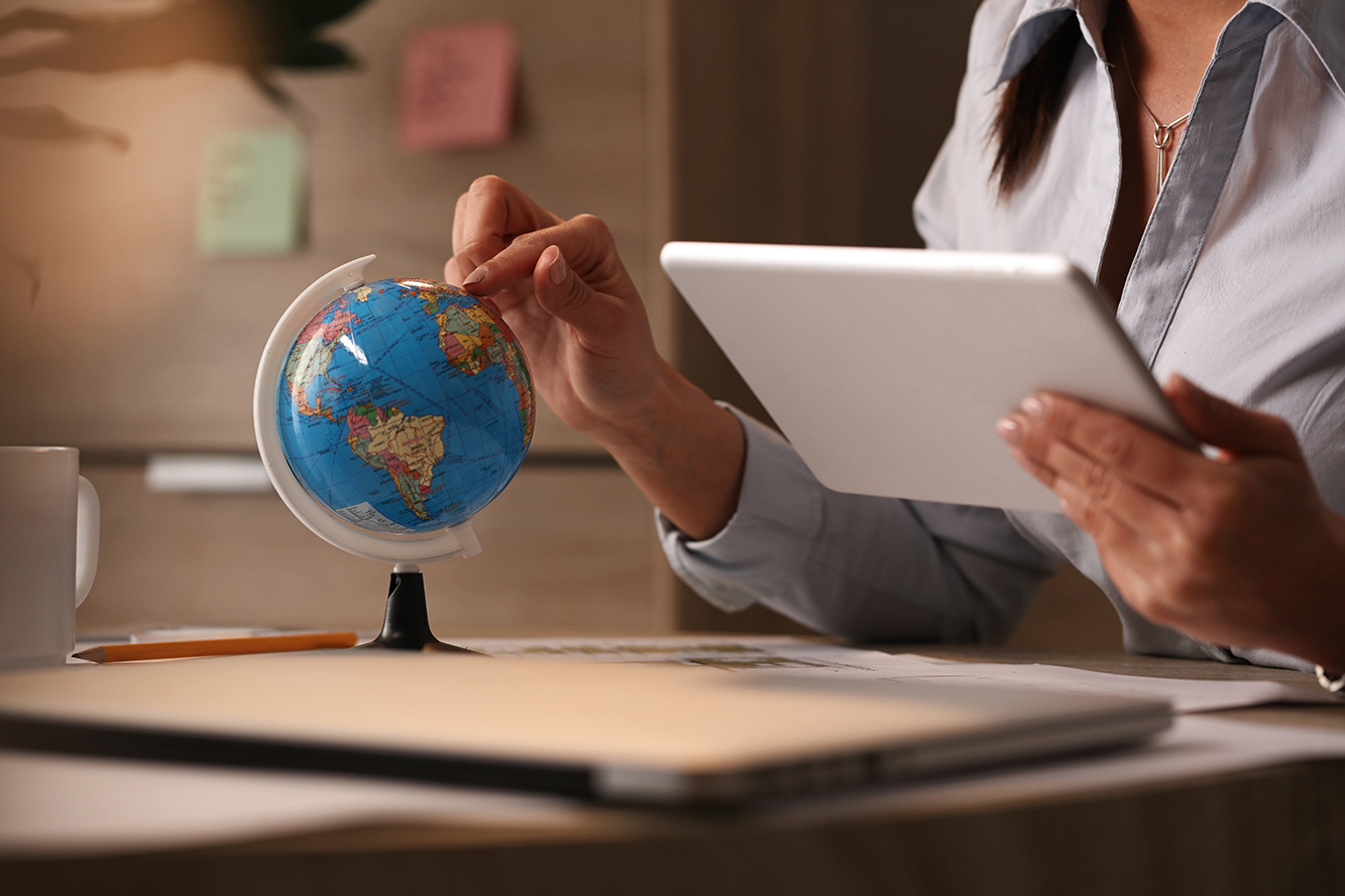 Profissional com tablet estuda mapa-múndi em ambiente de escritório.